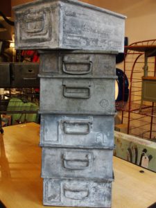Une pile de cinq boîtes de rangement rétro en métal avec poignées, placées sur une surface en bois dans un décor intérieur, dégage le charme Brocante.