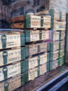 Caisses militaires en bois empilées avec des marquages indiquant les types et les quantités de munitions, exposées à l'intérieur d'un magasin de brocante, donnant un charme vintage.