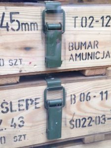 Des piles de caisses en bois vintage avec des marquages militaires, des fermoirs métalliques et des textes incluant « 45 mm » et « Bumar Amunicja » évoquent un charme rétro.