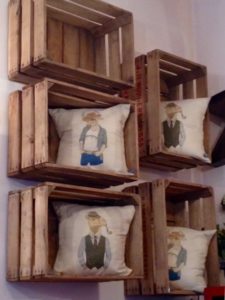Quatre caisses en bois fixées au mur, chacune contenant un oreiller avec des illustrations d'animaux élégamment habillés, confèrent une touche de charme vintage à la pièce.