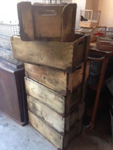 Une pile de cinq caisses en bois rustiques dans une zone de stockage avec d'autres caisses de brocante en arrière-plan.