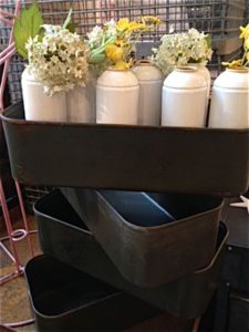 Trois conteneurs métalliques rétro empilés contiennent des vases blancs avec des fleurs blanches et jaunes.