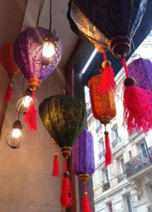 Des lanternes vintage colorées avec des pampilles sont suspendues au plafond près d'une fenêtre, complétées par un fond brocante représentant une rue et des bâtiments de la ville.