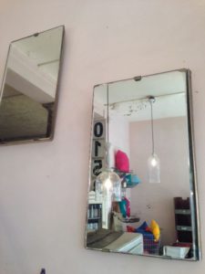 Deux miroirs rectangulaires suspendus vintage reflètent une pièce avec des coussins colorés, une suspension et une poutre de plafond authentique.