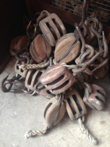 Une pile de poulies et de cordes en bois d'époque sur un sol en béton, avec quelques crochets et chaînes en métal rétro intercalés.