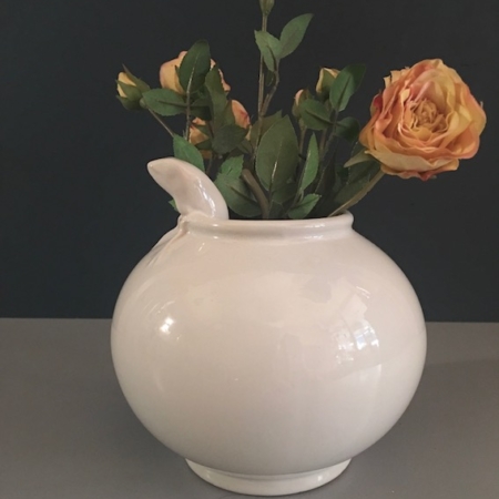 Vase en céramique blanche Porcelaine Grenouille à bec verseur, tenant des roses oranges et des tiges vertes, sur fond sombre, évoque l'allure charmante de la brocante 93. Brocante 93