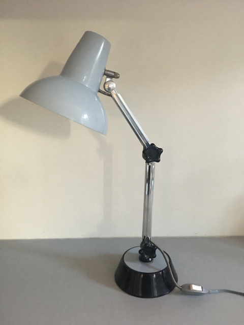 La Lampe de Bureau 1960, dotée d'une lampe réglable grise et d'une base noire associée à un cordon d'alimentation, est posée sur une surface grise, ajoutant une touche de charme brocante au décor. Brocante 93