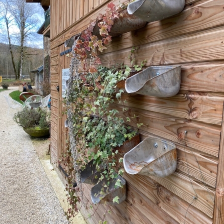 Coupelles à Grain XL 1960 montées sur un mur en bois présentent des plantes en cascade le long de l'allée d'un charmant bâtiment en bois, évoquant une ambiance rétro. Brocante 93