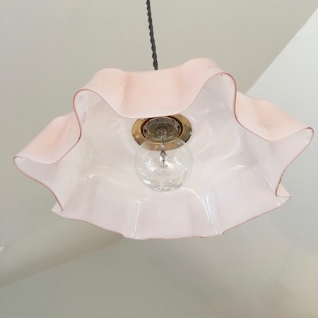 La Suspension Opaline Rose 1950 VENDU est un luminaire suspendu d'inspiration brocante doté d'un abat-jour volanté en forme de fleur rose et blanc, avec une ampoule visible à l'intérieur. Brocante 93