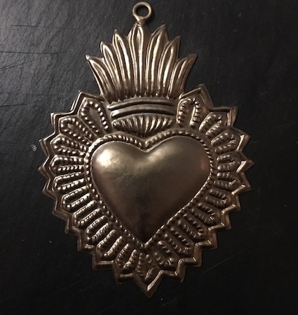 Un pendentif décoratif en forme de cœur en argent avec des motifs ornés sur fond noir, exsudant le charme intemporel de Coeur Dipika. Brocante 93