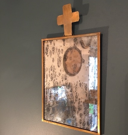 Le Miroir Jeanne, doté d'un cadre doré et d'une croix sur le dessus, projette un reflet vieilli et terni sur un mur vert, évoquant le charme des trésors de brocante. Brocante 93