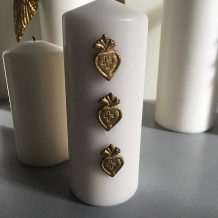 La bougie Bijoux de Bougies Coeurs arbore un extérieur blanc orné de trois symboles de cœur dorés alignés verticalement, évoquant le charme des trésors de brocante, et est représentée parmi d'autres élégantes bougies blanches. Brocante 93