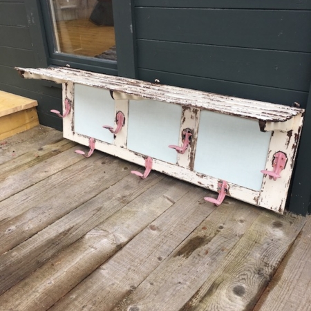 Le Porte-Manteaux & Chapeaux 1950 VENDU, avec sa finition blanche patinée et ses crochets roses, repose sur une terrasse en bois contre un mur vert foncé, dégageant une charmante ambiance vintage. Brocante 93