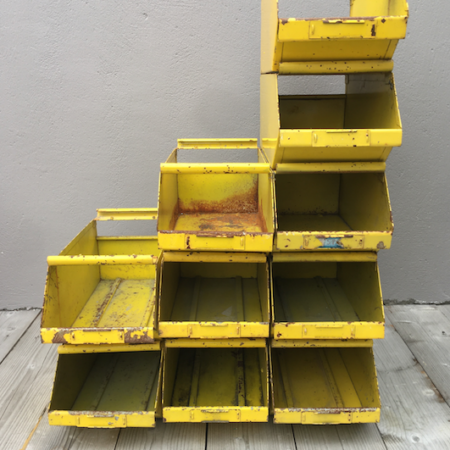 Une pile de Caisses Industrielles 1960 VENDSU en métal jaune repose sur une surface en bois contre un mur gris, rappelant une trouvaille de brocante 93. Brocante 93