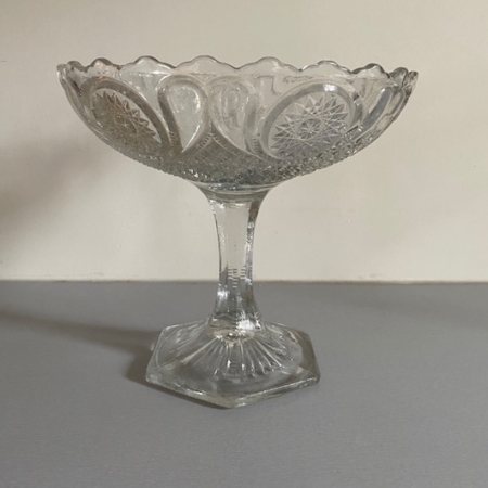 La « Coupe en Verre 1950 Motifs Géométriques Vendu », un plat à compote en verre vintage transparent et orné, doté d'une base piédestal et de bords festonnés, repose élégamment sur une surface unie. Brocante 93