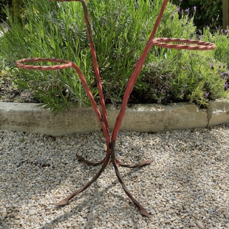 Porte-Plantes 4 pots 1960, doté d'une construction en métal vintage avec des branches rouges rouillées et de multiples supports circulaires, est élégamment placé sur une surface de gravier dans un jardin. Brocante 93