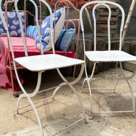 Deux Paires de Chaises Fer Forgé 1950 VENDU, au charme rétro, sont disposées sur une terrasse extérieure près d'un canapé rose orné de coussins à motifs bleus et blancs. Brocante 93