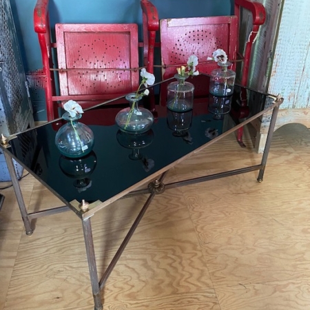 Une Table Basse vintage 1960 avec un plateau en verre présente trois élégants vases en verre, chacun contenant une fleur blanche, et se dresse fièrement devant deux chaises en bois rouge. Brocante 93