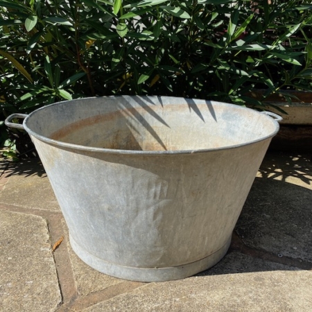 La Bassine Ronde 1960 GM trône sur un patio en pierre avec des plantes vertes feuillues en arrière-plan, ajoutant une charmante touche rétro à la scène. Brocante 93