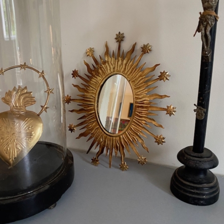 Miroir Céleste Or, crucifix noir et un coeur doré vintage avec des épines enfermés dans du verre sur une surface gris clair. Brocante 93