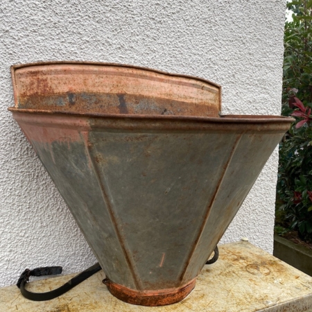 La Hotte de Vigneron 1960, objet vintage en métal rouillé de forme conique avec sangles, repose contre un mur blanc dégageant un charme désuet. Brocante 93