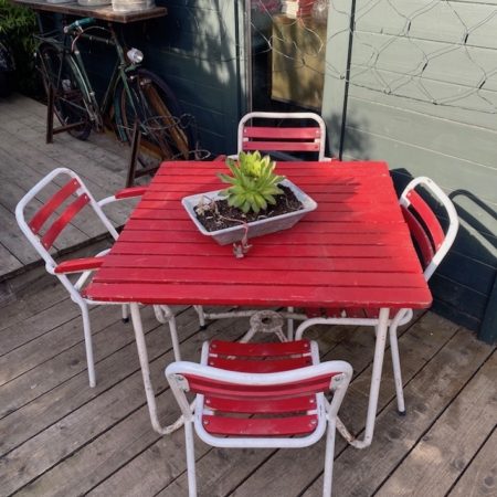 L'Ensemble de Jardin 1950, composé d'une table d'extérieur rouge et blanche avec une pièce maîtresse verte en forme de succulente, placée à côté d'un vieux vélo et d'arrosoirs vintage, dégage une charmante ambiance rétro. Brocante 93