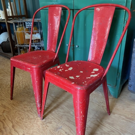 Deux Paires de Chaises Tolix 1950 VENDU usées et peintes en rouge écaillées, posées sur un plancher en bois, évoquent une charmante ambiance rétro. Un meuble vert en arrière-plan ajoute à l'ambiance vintage. Brocante 93