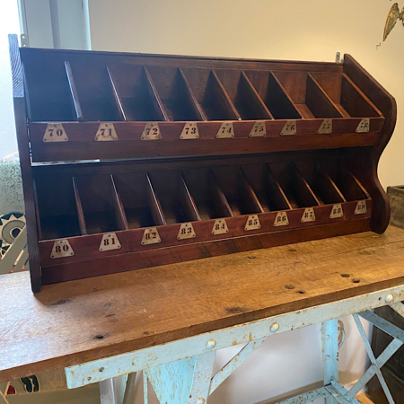 Le Meuble de Métier 1960 VENDU, un organiseur vintage en bois à compartiments numérotés, trône gracieusement sur une table en bois contre un mur, dégageant une charmante esthétique rétro. Brocante 93