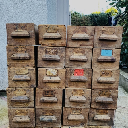 Ajoutez une touche de charme rétro à votre espace avec le Lot de Tiroirs 1960Gm VENDU, un ensemble de 24 tiroirs de rangement en bois vintage, chacun étiqueté de chiffres et de lettres usés, empilés à l'extérieur contre un mur. Disponible exclusivement chez Brocante 93. Brocante 93