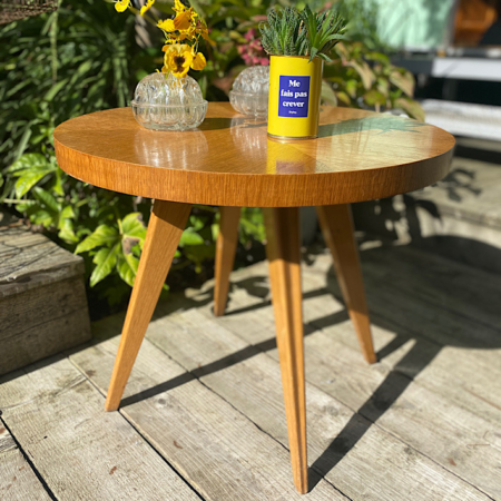 Une Table Basse 1960 VENDU en extérieur, ornée de fleurs dans des vases et d'une tasse bleue sur laquelle est écrit "Ne fais pas exprès", évoque une charmante ambiance rétro rappelant la brocante 93. Brocante 93