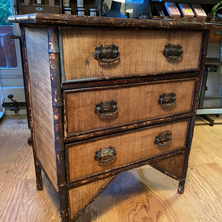 La Commode Bambou 1930 VENDU, une commode vintage en bois avec une finition vieillie et des poignées en laiton, ajoute un charme rétro à une pièce cosy avec parquet. Brocante 93