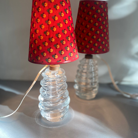 Deux lampes de table en verre des années 1960 avec des abat-jour à motifs rouges vifs sont positionnées sur une surface grise, projetant une lumière douce. Paire de Lampes 1960 VENDU.