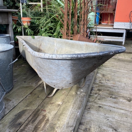 Une Baignoire Galva 1960 sur une terrasse en bois, entourée de verdure et d'outils de jardinage vintage. Brocante 93