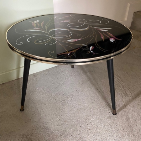 La table Guéridon Bas 1950 VENDU est une table ronde vintage avec un plateau en verre noir au design floral et trois pieds élancés, parfaite pour ajouter une touche de charme rétro à votre espace. Brocante 93