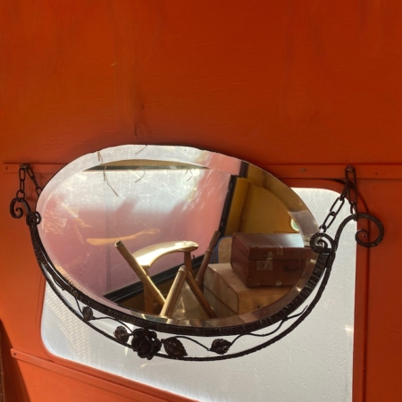 Le Miroir Fer Forgé 1950 avec son cadre noir décoratif est accroché sur un mur orange vif, reflétant une fenêtre et une partie de la pièce, dégageant un charme vintage. Brocante 93