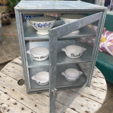 Un meuble Garde-Manger 1960 VENDU, mettant en valeur des bols décoratifs agrémentés de textes et de dessins, trône gracieusement sur une table en bois à l'extérieur, ajoutant une touche de charme rétro rappelant la brocante 93. Brocante 93