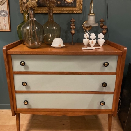 La Commode Pieds Compas 1960 est une commode vintage en bois à trois tiroirs, ornée de vases, de figurines et d'un petit tableau encadré au-dessus. Cette pièce rétro ajoute une touche de charme brocante à n'importe quel espace. Brocante 93