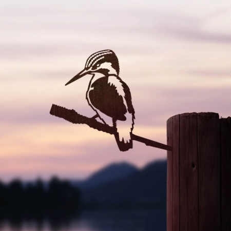 Le produit « Le Martin Pêcheur » présente la silhouette d'un oiseau perché sur un poteau en bois avec un lac tranquille et un coucher de soleil doux et pastel en arrière-plan, évoquant un charme vintage rappelant les cartes postales rétro. Brocante 93