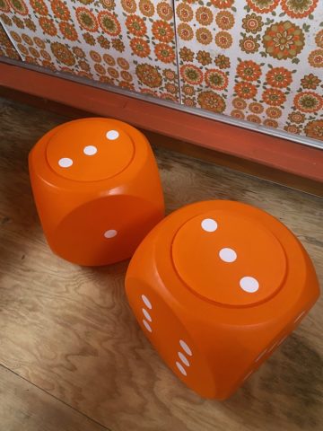 Deux grandes Boites Dés 1970, orange à pois blancs, reposent sur un plancher en bois contre un mur à motifs floraux rétro, dégageant une charmante ambiance vintage. Brocante 93