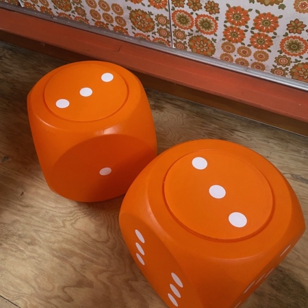 Deux grandes Boites Dés 1970, orange à pois blancs, reposent sur un plancher en bois contre un mur à motifs floraux rétro, dégageant une charmante ambiance vintage. Brocante 93