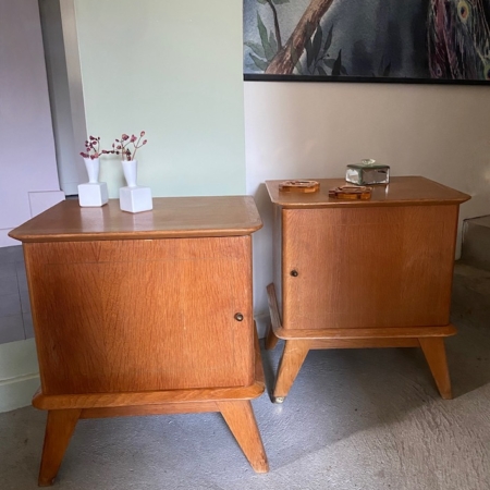 La Paire de Chevets 1960 VENDU, deux tables d'appoint rétro en bois comportant chacune une porte, sont joliment ornées de petits objets et de vases. Un tableau est suspendu au-dessus, renforçant le charme brocante 93. Brocante 93