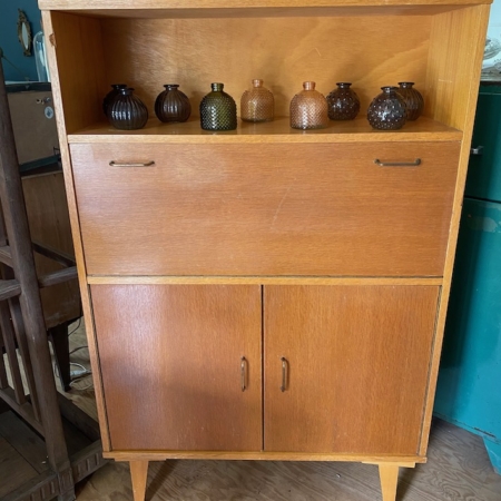 Secrétaire vintage 1960 en bois avec deux compartiments fermés en bas et six vases en verre texturé sur l'étagère ouverte, ajoutant une touche de charme rétro. Brocante 93