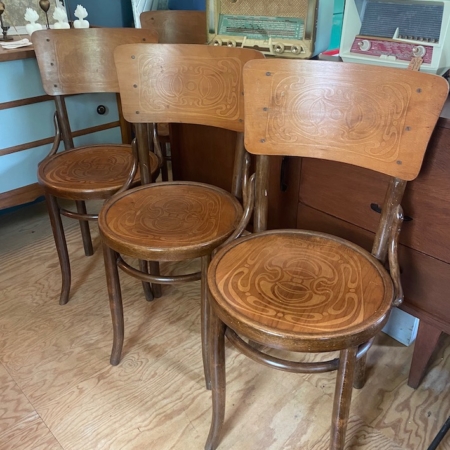 Trois Chaises Américaines 1940 aux dossiers et assises sculptées, rappelant le style Américaines des années 1940, disposées en enfilade sur un parquet en bois.