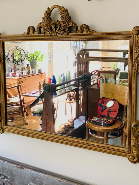 Le Miroir Mouluré Ancien XIXème reflète magnifiquement une pièce à l'ambiance rétro, mettant en valeur un métier à tisser, des meubles en bois et un ensemble de plantes en pot. L'ambiance générale évoque le charme classique de la Seine-Saint-Denis, 93.