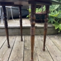 La Table à rabats 1940, dotée de pieds tournés et ouvragés des années 40, est posée sur une terrasse en bois entourée de plantes et de mobilier d'extérieur. Brocante 93