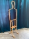 Valet de Chambre 1970, un porte-manteau abstrait en bois de forme humaine avec une étagère intégrée, se dresse élégamment contre un rideau bleu sarcelle foncé. Brocante 93