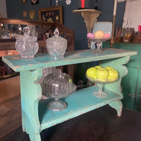 L'étagère « Etagère Primitive Style USA 1930 », une étagère vintage en bois bleu sarcelle, présente des récipients en verre, des objets décoratifs, des pommes vertes et des macarons dans une pièce chaleureuse au style primitif. Brocante 93