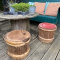 Espace extérieur avec tabourets en bois, table à enrouleur de câbles, plantes en pot et banc vert avec coussins rayés. L'espace s'inspire du Fût à Saké Japonais 1960, ajoutant une touche élégante. Brocante 93