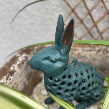 Le Photophore Lapin, une sculpture en métal bleu sarcelle dotée d'un corps perforé, est nichée parmi les plantes vertes du jardin, servant à la fois de pièce décorative enchanteresse et de photophore charmant lorsqu'il est illuminé. Brocante 93