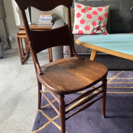 Une chaise de bureau américaine des années 1930 repose gracieusement sur un tapis violet près d'une table basse, avec un canapé et un coussin à pois en arrière-plan, ajoutant une touche de charme américain classique. Brocante 93